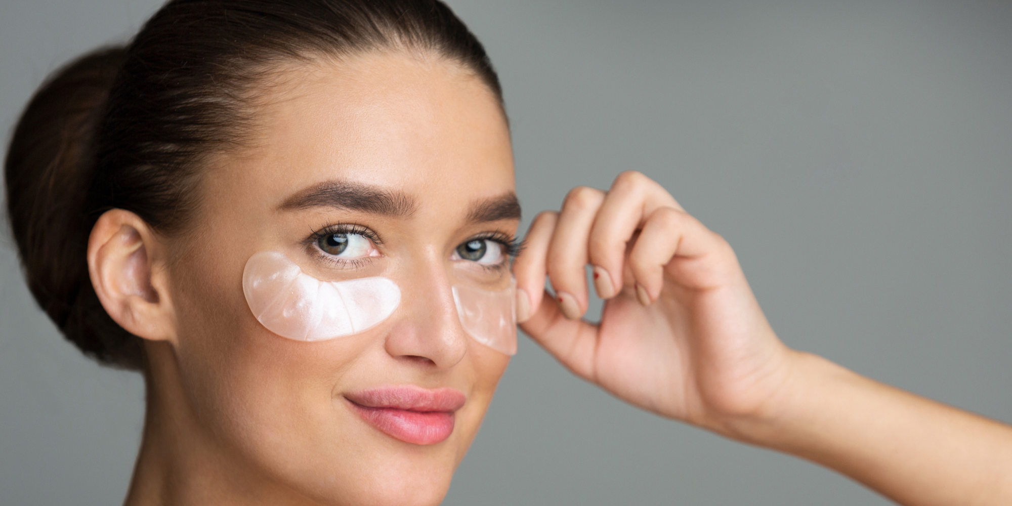 Woman applying eye patches on a gray background